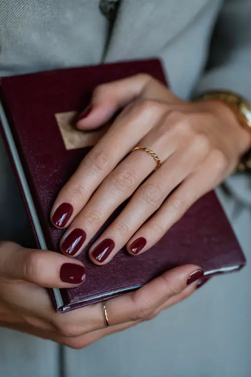 Matte burgundy nails with minimal gold line art, guest holding a wedding program
