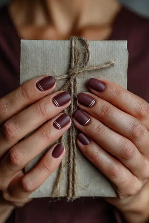 Matte plum nails with elegant gold striping, bride holding a rustic wedding invitation tied with ribbon 