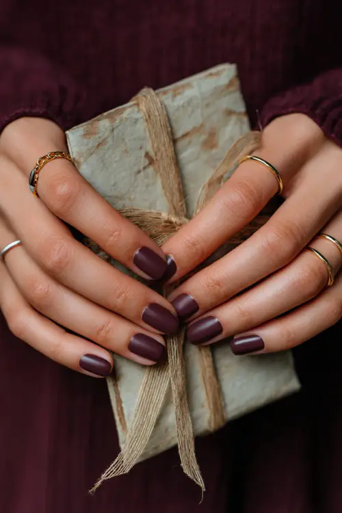 Matte plum nails with elegant gold striping, bride holding a rustic wedding invitation tied with ribbon 
