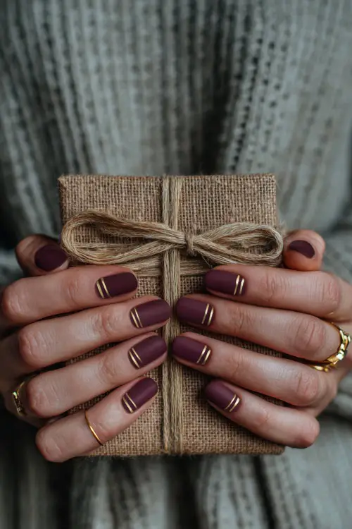Matte plum nails with elegant gold striping, bride holding a rustic wedding invitation tied with ribbon 