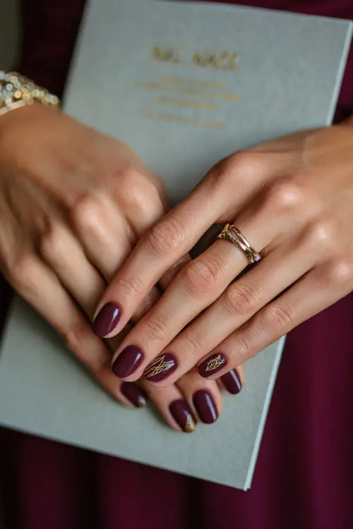 Matte plum short nails with delicate line art in gold, bridesmaid holding a wedding program card 