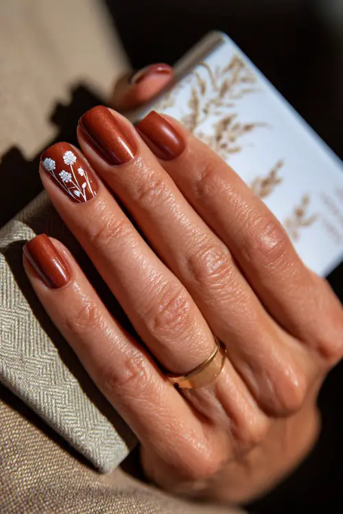 Matte rust nails with delicate white floral line art, bridesmaid holding a wedding program booklet 