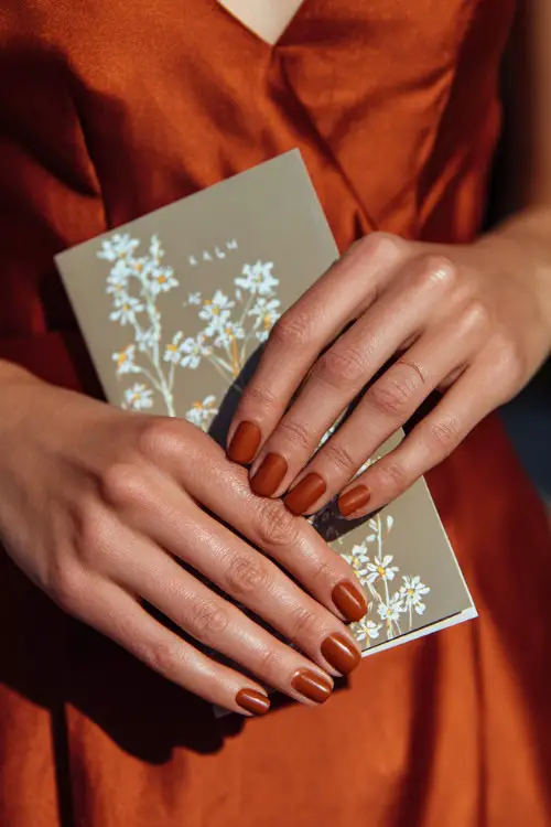 Matte rust nails with delicate white floral line art, bridesmaid holding a wedding program booklet