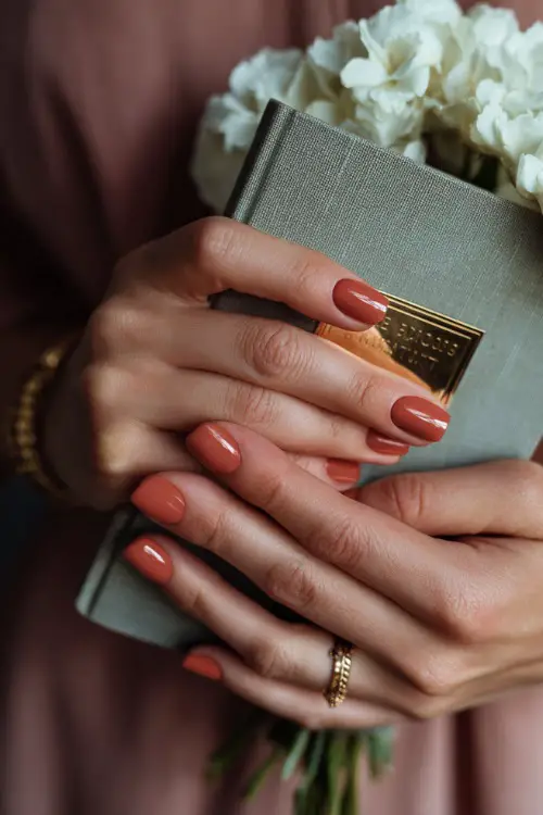 Matte terracotta nails with delicate floral line art, bridesmaid holding a wedding program booklet 
