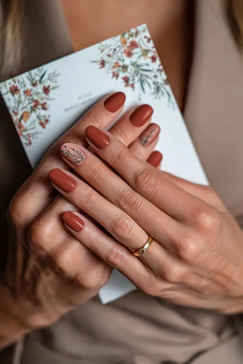 Matte terracotta nails with delicate floral line art, bridesmaid holding a wedding program booklet 