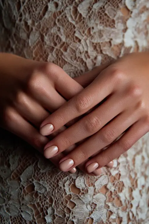Neutral warm beige nails with soft shimmer, guest’s hands placed over a lace dress
