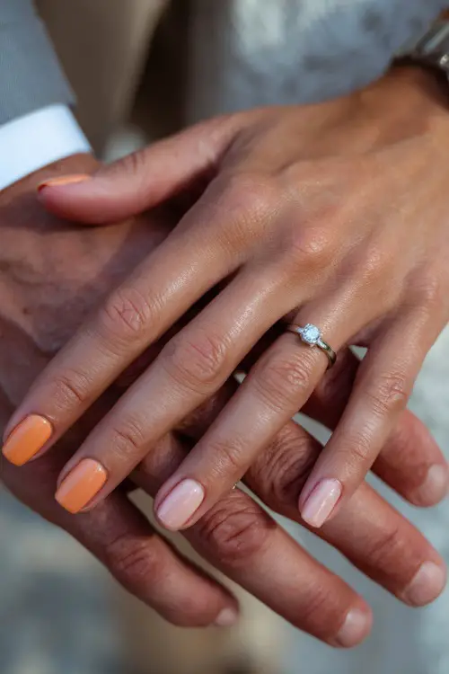 Ombré nails blending burnt orange and pale peach shades, bride’s hands intertwined with groom’s, wedding ring in focus 