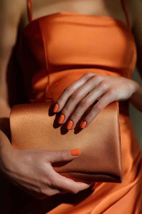 Ombré nails fading from peach to burnt orange, bridesmaid holding a satin clutch bag 
