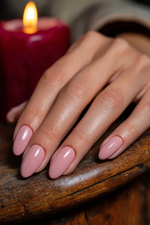 Pale pink nails in oval shape with a smooth glossy finish, guest’s hand resting on wooden wedding table with candles 