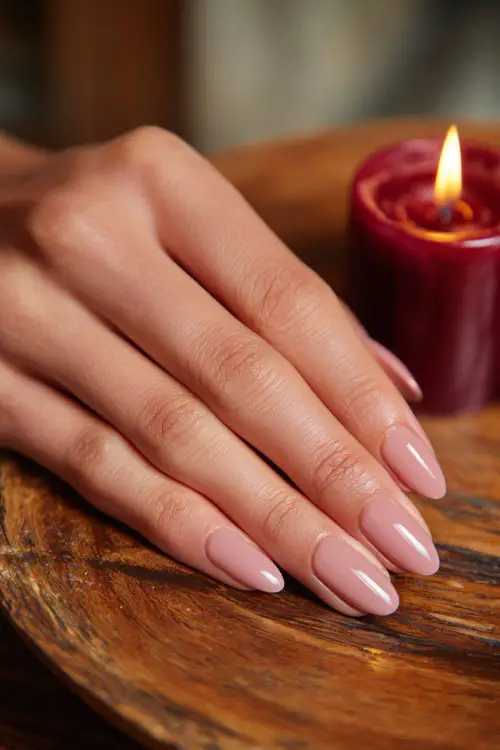 Pale pink nails in oval shape with a smooth glossy finish, guest’s hand resting on wooden wedding table with candles