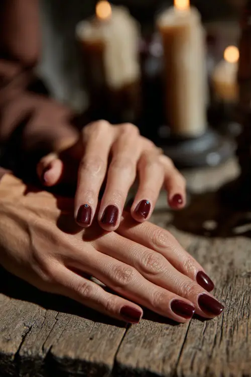Plum nails with small rhinestone accents, guest’s hands resting on a wooden wedding table decorated with candles 