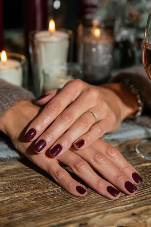 Plum nails with small rhinestone accents, guest’s hands resting on a wooden wedding table decorated with candles
