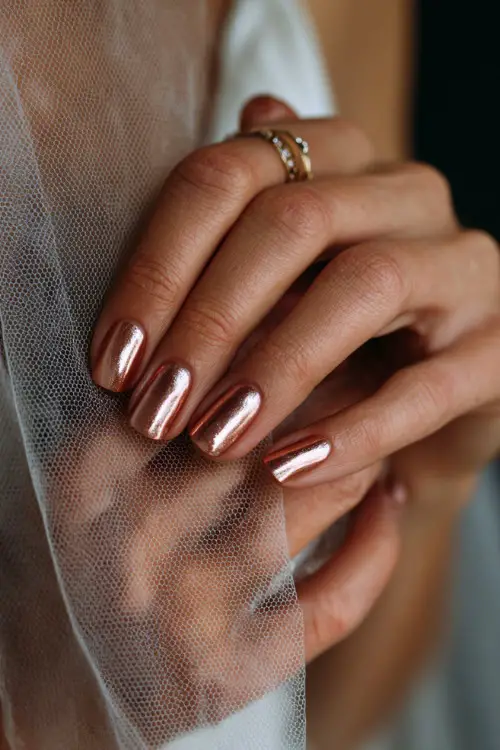 Rose gold chrome nails with fine rhinestone details, bride’s hands adjusting a sheer bridal veil