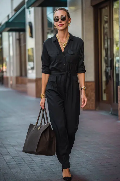A woman in her 40s wears a tailored black jumpsuit with a cinched waist and gold jewelry