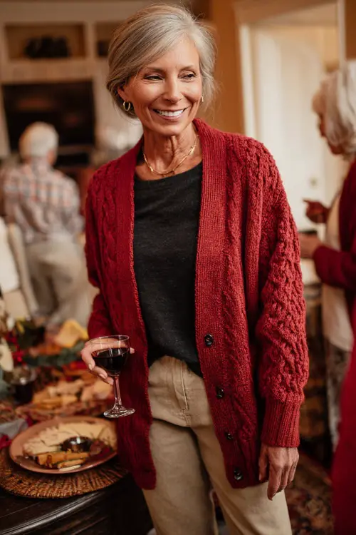 A woman over 50 in a red cardigan layered over a simple black top with straight-leg jeans and loafers, enjoying a relaxed holiday party with friends 