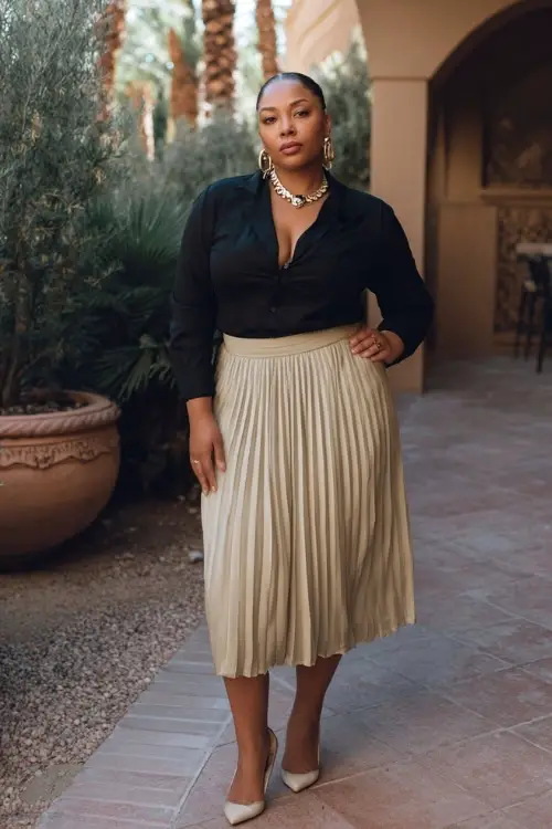 A curvy woman wears a formal boho ensemble combining a pleated chiffon midi skirt, a fitted long-sleeve blouse, elegant heels, and bold jewelry