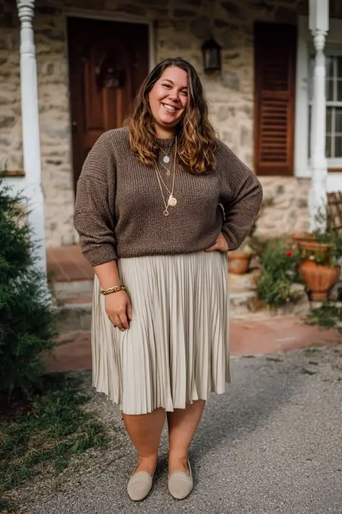 A plus-size woman wears a cozy boho outfit with a lightweight sweater tucked into a pleated midi skirt, comfortable flats, and layered necklaces 