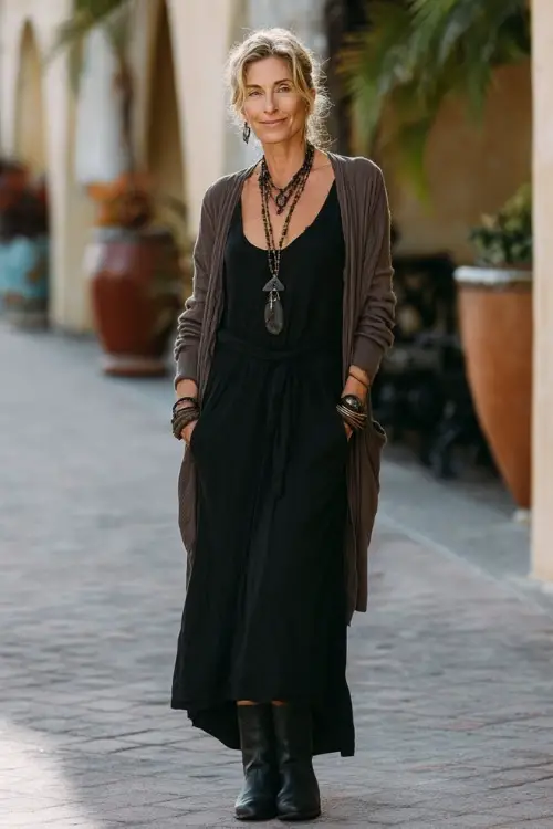 A woman over 50 wears a sophisticated boho outfit featuring a monochrome maxi dress, a lightweight cardigan, ankle boots, and a long necklace