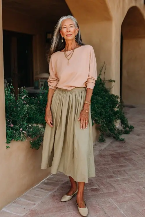 A woman over 50 wears an easygoing boho look featuring a soft knit top tucked into a flowy midi skirt, comfortable flats, and subtle jewelry