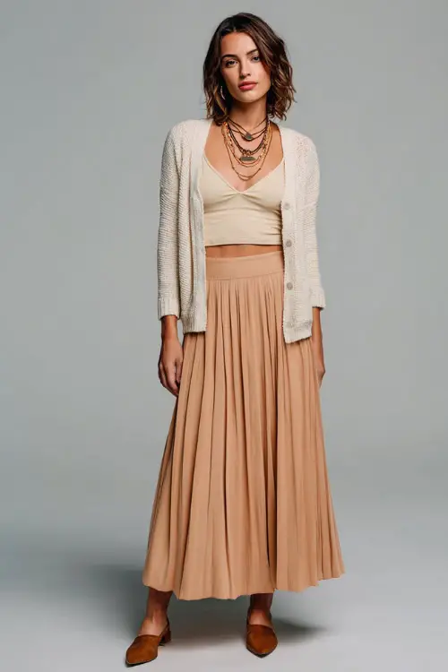 A woman wears an office-appropriate boho outfit with a long pleated skirt, a soft knit top, a cropped cardigan, and closed-toe pumps 