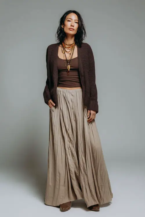 A woman wears an office-appropriate boho outfit with a long pleated skirt, a soft knit top, a cropped cardigan, and closed-toe pumps 