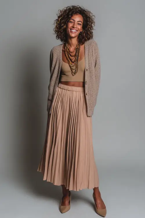 A woman wears an office-appropriate boho outfit with a long pleated skirt, a soft knit top, a cropped cardigan, and closed-toe pumps