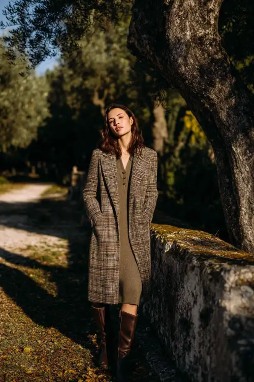 A woman over 30 wears a plaid wool coat over a fitted knit dress with Chelsea boots, standing in an autumn park, full-body fashion photography, soft seasonal light