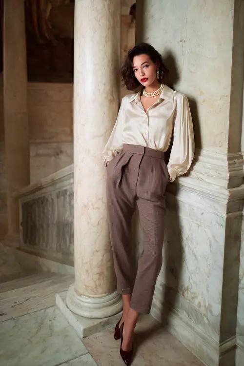 A woman wears structured classic trousers with a silk blouse, pearl accessories, low heels, standing on marble steps of a historic building, full-body fashion photography