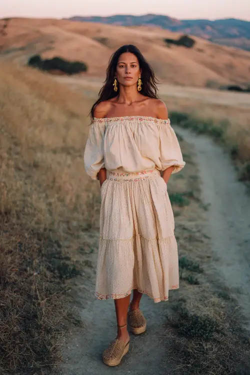 A woman over 40 wears an off-shoulder boho blouse with delicate embroidery and a tiered midi skirt, paired with espadrille wedges and statement earrings