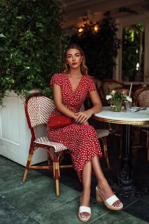 Full body editorial fashion photograph of a poised woman wearing a timeless red and white polka dot wrap midi dress with cap sleeves 