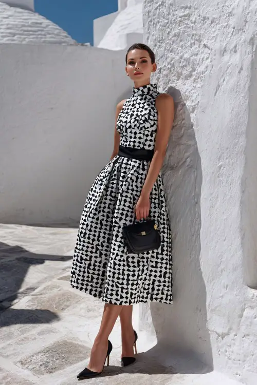 Full body editorial fashion photograph of an elegant woman wearing a classic black and white geometric print sleeveless midi dress with a fitted bodice and flared skirt 