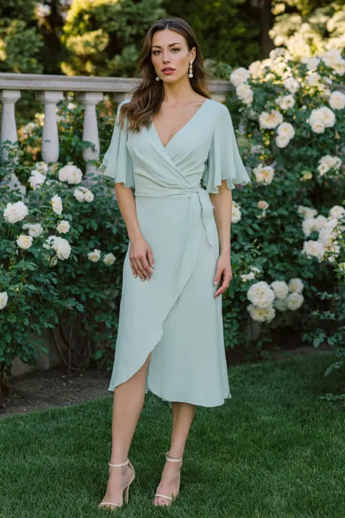 Full body editorial shot of a sophisticated woman wearing a classic pastel mint green chiffon wrap midi dress with delicate flutter sleeves and a V-neckline