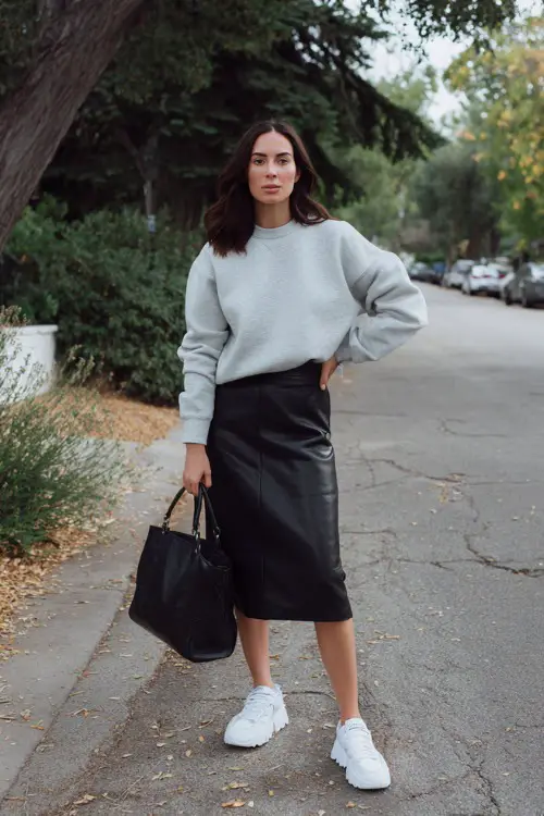 Full body fashion photograph of a casual chic woman dressed in a classic oversized soft grey crewneck sweatshirt tucked loosely into a high-waisted black tailored midi skirt 