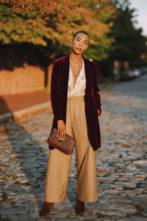 a sophisticated, radiant woman with a sleek dark lob haircut wearing a rich burgundy velvet kimono jacket over a cream silk blouse and wide-leg tailored trousers in warm camel