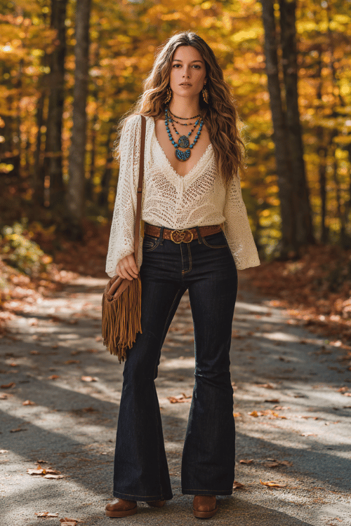 a woman wearing a loose cream crochet top tucked into high-waist flared dark wash jeans, a wide brown leather belt, layered turquoise and gold pendant necklaces