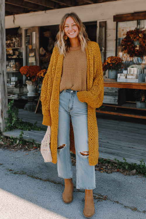 a woman wearing an oversized mustard yellow knit sweater with dropped shoulders over wide-leg light wash jeans with subtle distressing, a long open-front boho cardigan in warm oatmeal tones