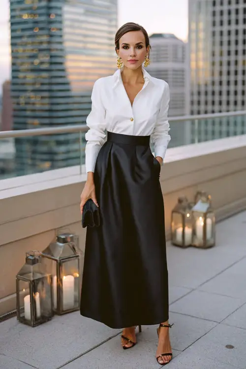 an elegant woman dressed in a classic crisp white tuxedo shirt with French cuffs and gold cufflinks tucked into a high-waisted floor-length satin skirt in deep midnight black 