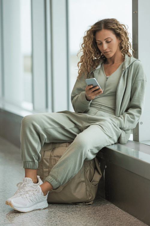 woman in a buttery soft lounge set a long-sleeve zip-up top and matching tapered jogger pants in sage green with cushioned white running sneakers and a spacious canvas tote 