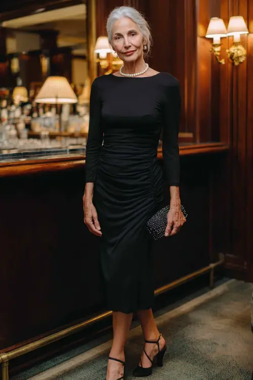 woman over 50 wearing a classic fitted long-sleeve midi dress in timeless black crepe with subtle ruched detailing at the waist and an elegant modest neckline