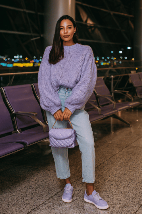 woman wearing a soft lavender oversized knit sweater with balloon sleeves tucked loosely into high-waist straight-leg light wash jeans, with lilac leather sneakers 