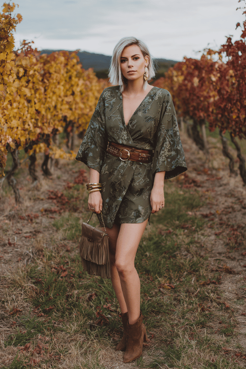 woman with a sleek silver lob haircut wearing a deep olive wrap dress with botanical print and flutter sleeves, a structured leather belt, stacked gold bangles and drop earrings