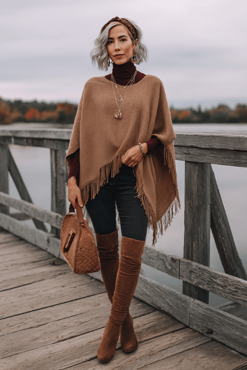 woman with salt and pepper shoulder-length hair wearing a luxurious camel-toned fringed poncho over a fitted dark burgundy turtleneck and straight-leg dark wash jeans