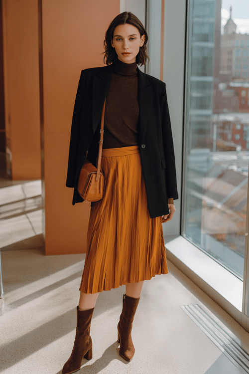 a woman wearing a rich espresso brown mock-neck sweater tucked into a high-waisted pleated skirt in warm rust-orange, layered with a fitted black blazer, finished with block-heel ankle boots