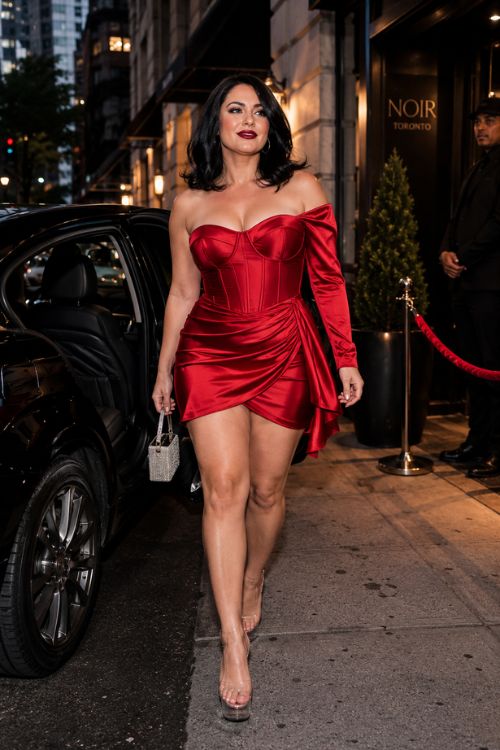 A curvy woman wears a red off-the-shoulder satin mini dress with clear heels