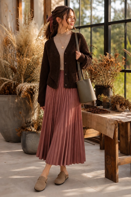 a woman wears a fall old money outfit with a brown cardigan, beige turtleneck, pleated mauve midi skirt, and taupe loafers