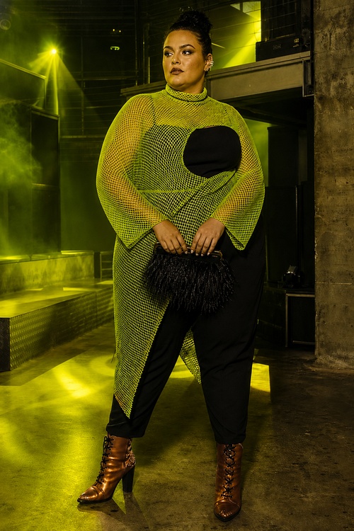 a woman wears a neon mesh overlay with a black jumpsuit, bronze lace-up boots, and a feather clutch