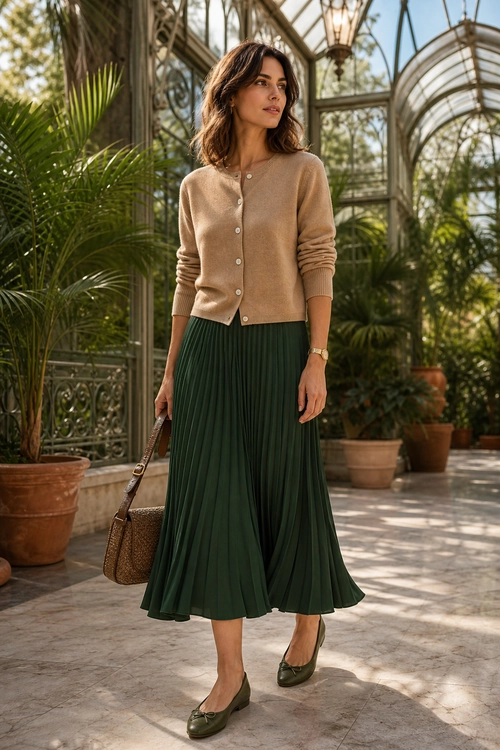 Beige Cardigan and Green Pleated Skirt Outfit A woman wears a beige button-front cardigan with a dark green pleated skirt, olive loafers, and a brown shoulder bag.