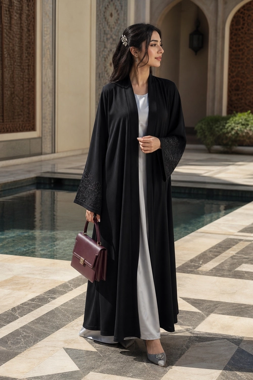 Black Abaya with White Dress A woman wearing a flowing black abaya over a white dress with gray pointed flats and carrying a burgundy handbag.
