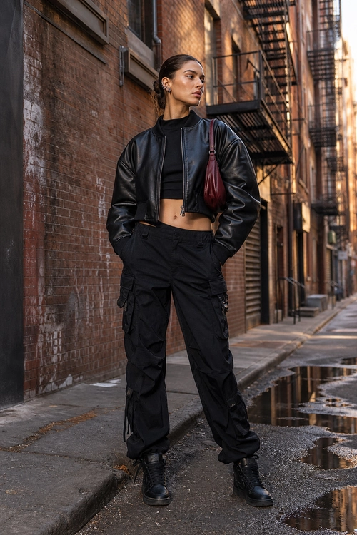 An all-black outfit featuring a cropped leather jacket, crop top, cargo pants, combat boots, and a burgundy shoulder bag.