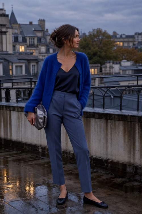 Blue Cardigan and Tailored Trousers A woman wears a cobalt blue cardigan over a black camisole with blue-gray tailored trousers, black loafers, and a metallic clutch.